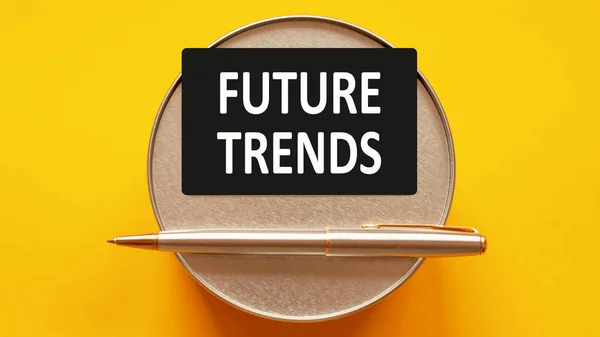 FUTURE TRENDS - words writing a white letters on a sheet paper. Black card with text on a yellow background with round metal stand and metal writing pen. Business, finance and education concept