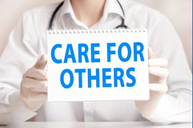 Doktor elinde beyaz bir kart tutuyor ve diğerlerini önemseyen kelimeleri işaret ediyor. Hastane, klinik ve tıbbi otobüsler için sağlık hizmetleri kavramı.