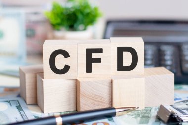 The letters CFD written on wood cubes. Pen, banknotes, calculator and green plant in a flower pot on the background. CFD - short for Contract For Difference, business concept. clipart