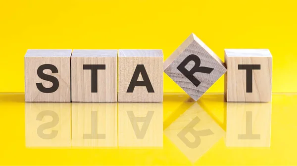 start word written on wood block. start word is made of wooden building blocks lying on the yellow table. Business concept