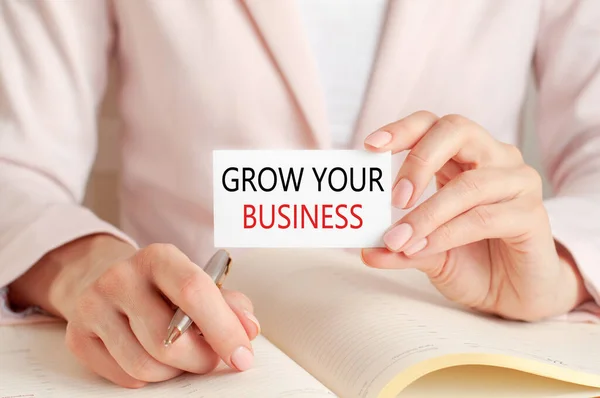 女人用银笔写在笔记本上 手里拿着写着 扩大你的生意 粉色背景 前景色 商业和教育概念 — 图库照片