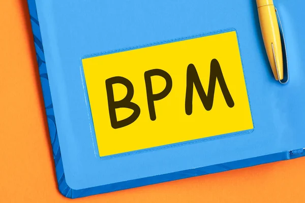 The letters bpm is written in black letters on yellow note paper. A yellow pen is embedded in the background of the blue diary.