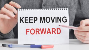 Adam gümüş bir kalem ve el ele tutuşma kartıyla bir deftere şöyle yazmış: Devam edin. Gri arka plan, ön manzara. işletme ve eğitim kavramı.