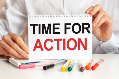 Beyaz gömlekli bir adam elinde bir kağıt parçası tutuyor: eylem zamanı. Masada çok renkli kalemler ve tablet var. İş ve eğitim kavramı