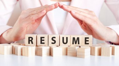 İş kadını, özgeçmiş sözcüğüyle ellerini tahta küplerin üzerinde tutuyor. Kelime, masanın beyaz yüzeyinde duran pembe arka planda duran tahta küplere yazılmıştır..