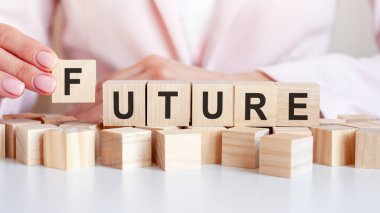 El, F ahşap küpü ve FUTURE harfini koyuyor. Kelime, masanın beyaz yüzeyinde duran pembe arka planda duran tahta küplere yazılmıştır..