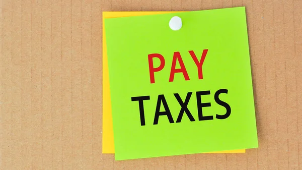 pay taxes written on green paper and pinned on corkboard, business concept