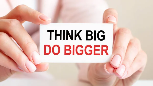 think big do bigger is written on a white business card in a woman\'s hands. Pink background. Business and advertising concept