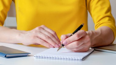 Beyaz, boş bir deftere yazan bir kadının yakın plan resmi. Sarı arka plan, seçici odaklanma. İş, pazarlama, eğitim, finansal konsept için kullanılabilir.