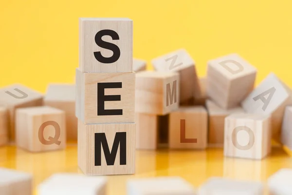 SEM - short for Search Engine Marketing - written on a wooden cube, business concept. yellow bacground. can be used for business, marketing, education, financial concept. Selective focus.