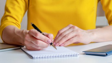 Beyaz, boş bir deftere yazan bir kadının yakın plan resmi. Sarı arka plan, seçici odaklanma. İş, pazarlama, eğitim, finansal konsept için kullanılabilir.