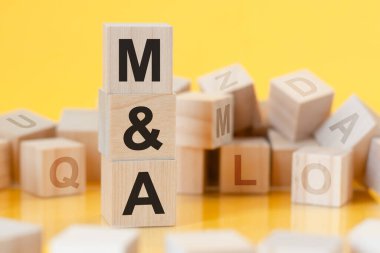 M and A - short for mergers and acquisitions - written on a wooden cube, business concept. yellow bacground. can be used for business, marketing, education, financial concept. Selective focus. clipart