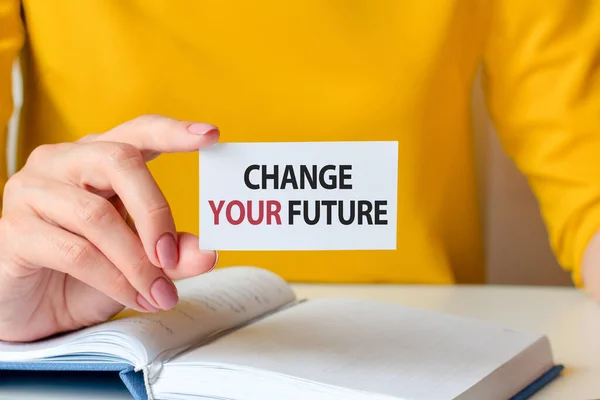 change your future is written on a white business card in a woman\'s hand. Yellow background. Business and advertising concept