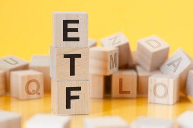 Dikey piramide yerleştirilmiş tahtadan küpler, sarı arkaplan, harflerle sıralanmış tahta küpler, masanın yüzeyinden yansıma, iş konsepti, ETF - Ticaret Fonu