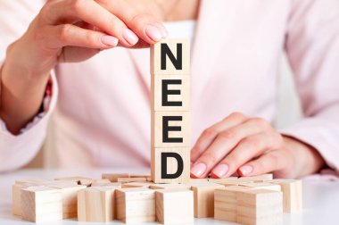 Pembe elbiseli kadın elinin arka planına karşılık kelime ihtiyacı olan dört tahta küp. İş, finans ve ekonomik konsept.