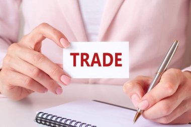 Kadın defterine gümüş bir kalem ve el ele tutuşma kartıyla yazı yazıyor: takas. Pembe arka plan, ön manzara. İş, finans ve eğitim konsepti için kullanılabilir.