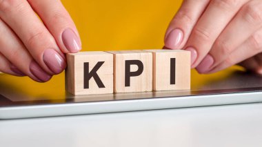 Kadın elleri not defterinin siyah yüzeyine KPI harfleriyle tahta bloklar koyar. İş, pazarlama, eğitim ve konsept için kullanılabilir. Sarı arka plan. kpi - Anahtar Performans Göstergeleri