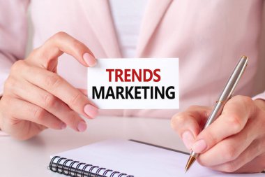 Kadın defterine gümüş bir kalem ve el ele tutuşma kartıyla yazıyor: trend pazarlama. Pazarlama, iş ve finans konularında kullanılabilir. Pembe arkaplan, ön görünüm.