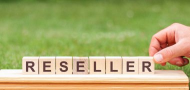 Reseller tahta bloklara yazılmış bir kelimedir. Bir adamın elinde yeşil çimenliğin arka planında 
