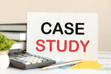 Üzerinde metin dosyası olan beyaz kart, dizilmiş kitapların, hesap makinesinin, kalemin, yeşil saksı bitkisinin arka planında duruyor. İş ve finansal konsept. Seçici odak.