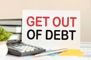 Metni olan beyaz kart, masanın üzerinde duran kitapların, hesap makinesinin, kalemin, yeşil saksı bitkisinin arka planında duruyor. İş ve finansal konsept. Seçici odak.