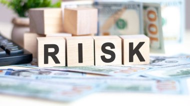 The word risk on wood cubes, banknotes and calculator on the background. Can be used for business, marketing and commerce concept
