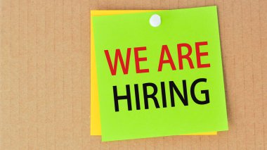 we are hiring written on green paper and pinned on corkboard, business concept