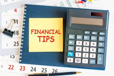 Metin finansal ipuçları ve hesap makinesi olan sarı bir kağıt parçası not defterinin üzerinde duruyor. Defter ve kalem, doküman sayfalarında yer alıyor. iş ve finansal konsept. seçici odak