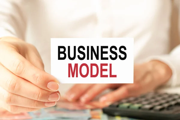 business model is written on a white business card. a woman's hand holds a white paper card, white background. business and advertising concept. defocus.