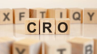 Üç oyuncak tahta blok ve üzerinde CRO harfleri var. Arka planı aydınlık, seçici odaklı. CRO - dönüştürme oranı optimizasyonunun kısaltılmışı