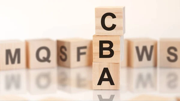 wooden cubes with word CBA arranged in a vertical pyramid, on the white background is a row of wooden cubes with letters, reflection from the surface , business concept. CBA - cost benefit analysis