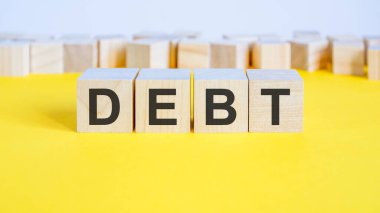 Tahta bloklardaki borç sözcüğü sarı masada yatıyor. Etrafında harfler olan iş konsepti oyuncak blokları. seçici odak