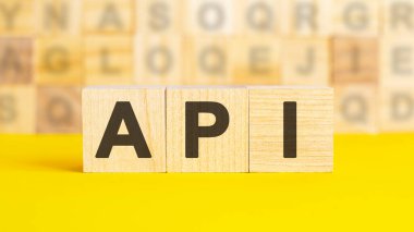 Metin API parlak sarı bir yüzeydeki tahta küplere yazılmıştır. Arka planda farklı harflerle yazılmış küpler var. İş konsepti. API - uygulama programlama arayüzünün kısaltması