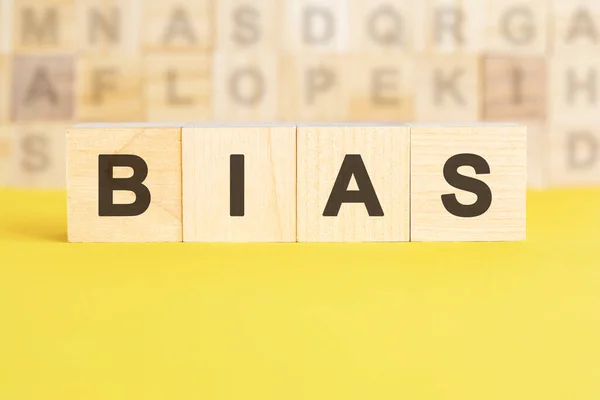 Stock image the word bias is written on wooden cubes on a bright yellow surface. in the background are rows of cubes with different letters. business and finance concept