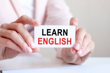 İngilizce 'nin bir kadının elindeki beyaz kartvizitte yazıldığını öğrenin. Pembe arka plan. İş ve reklam kavramı