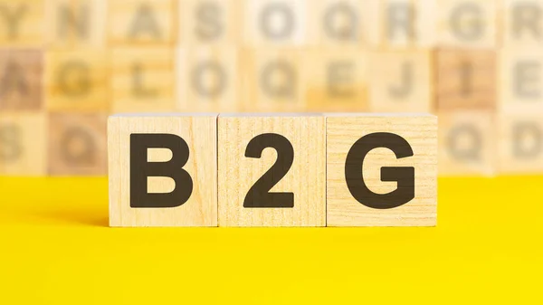 テキストB2Gは明るい黄色の表面に木製の立方体に書かれています 背景には異なる文字を持つ立方体の行があります ビジネスコンセプト B2G 政府へのビジネスのための短い — ストック写真