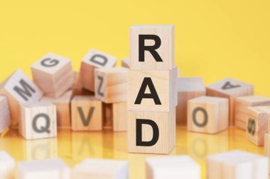 RAD harfli tahta küpler dikey piramit şeklinde dizilmiş, sarı arkaplan, masanın yüzeyinden yansıma, iş konsepti, RAD - hızlı uygulama geliştirmenin kısaltması