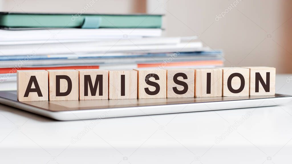 the word admission is written on wooden cubes standing on a notepad, in the background a stack of documents, selective focus. can be used for business, education, financial concept