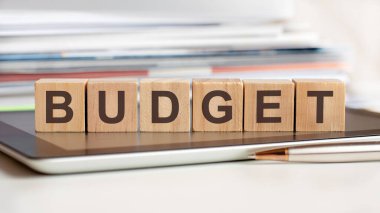 Bütçe kelimesi bir not defterinin üzerinde duran tahta küplere yazılmıştır. Arkaplanda seçici bir odak noktası olan bir yığın belge vardır. iş, eğitim, finansal konsept için kullanılabilir.