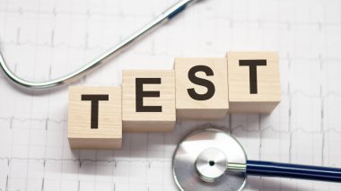 Tahta bloklara ve arka planda steteskopa yazılmış test sözcüğü. Hastane, klinik ve tıbbi otobüsler için sağlık hizmetleri kavramı