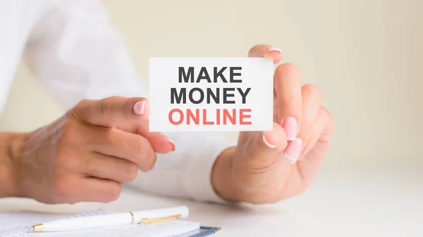 make money online words inscription on white card paper sheet in hands of woman. black and red letters on white paper. business concept, grey backgrond