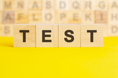 TEST kelimesi parlak sarı bir yüzeyde tahta küplere yazılır. Arka planda farklı harflerle yazılmış küpler var. iş ve finans kavramı