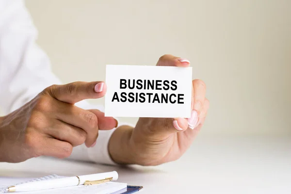 business assistance inscription on white card paper sheet in hands of woman. black and red letters on white paper. business concept, grey backgrond