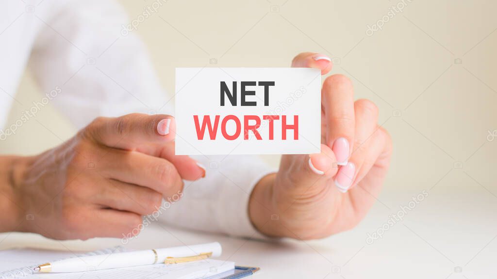 NET WORTH inscription on white card paper sheet in hands of woman. black and red letters on white paper. business concept, grey backgrond