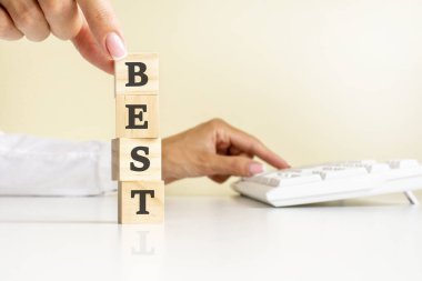 Beyaz tişörtlü, tahta bloklu, beyaz masa zemininde beyaz klavyeli en iyi ifade için elini kapat. finansal ve iş kavramları