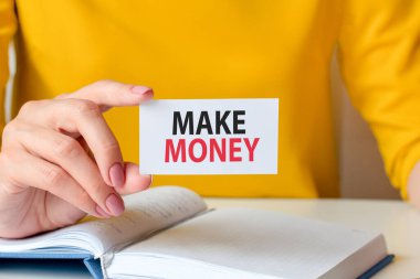 Para kazanmak beyaz kartvizitle yazılır. Sarı bir elbise ve beyaz bir defterin arka planında beyaz bir kağıt tutan bir kadın eli. İş ve reklam kavramı.