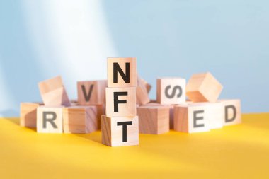 Üzerinde NFT harfleri olan tahta küpler dikey piramit, gri ve sarı arka plan, iş konsepti. NFT - geri ödemesiz jetonun kısaltması