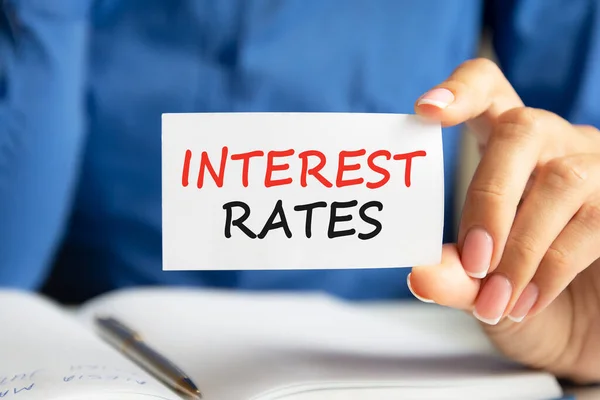 interest rates is written on a white business card in a woman\'s hand. Blue background. Business and advertising concept