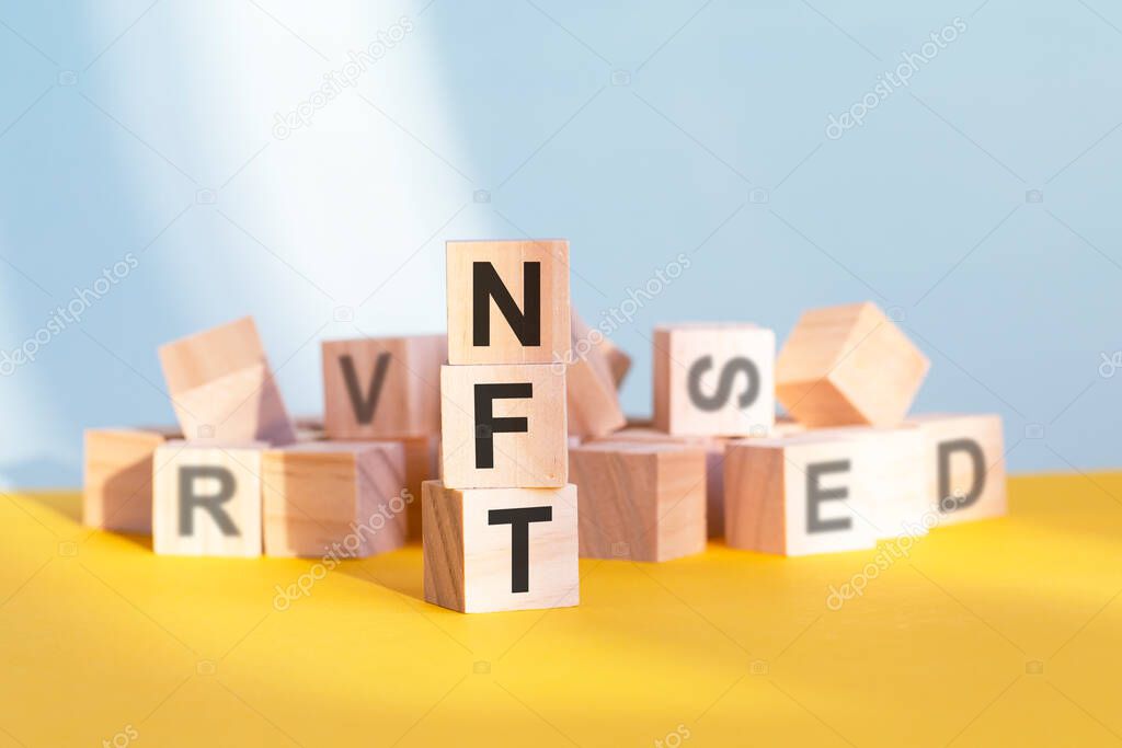 wooden cubes with letters NFT arranged in a vertical pyramid, grey and yellow background, business concept. NFT - short for non fungible token