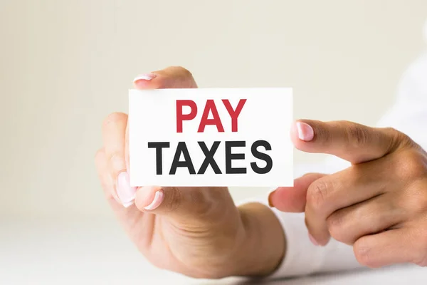 female hands hold card paper with text PAY TAXES - on a white light background. business and finance concept